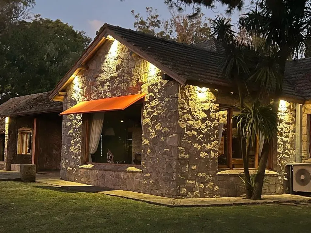 Hostería de piedra Los Nobles Art al atardecer, con sus ventanales iluminados y el parque